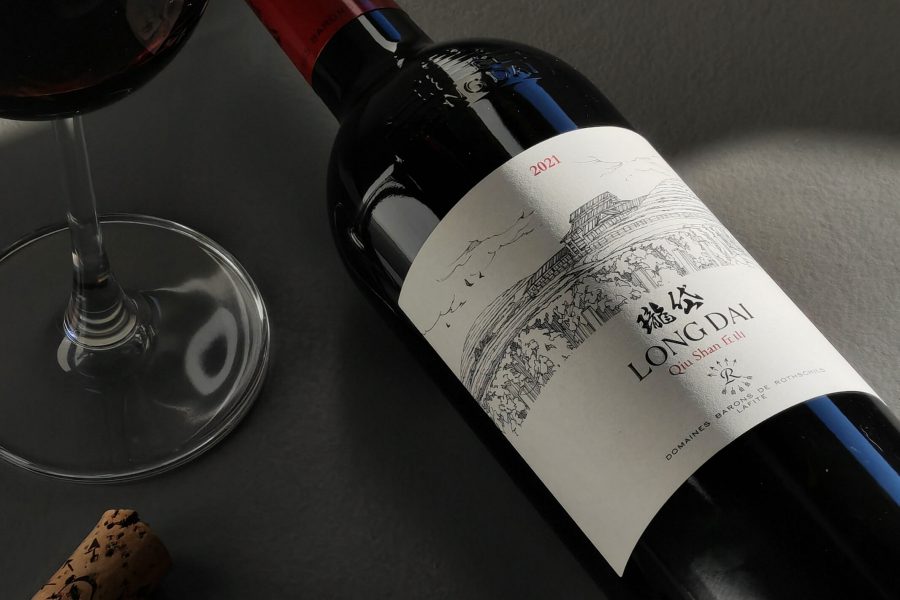 Close-up of a bottle of Long Dai, Qiu Shan Valley 2021 lying flat next to a glass of red wine and two wood corks.  